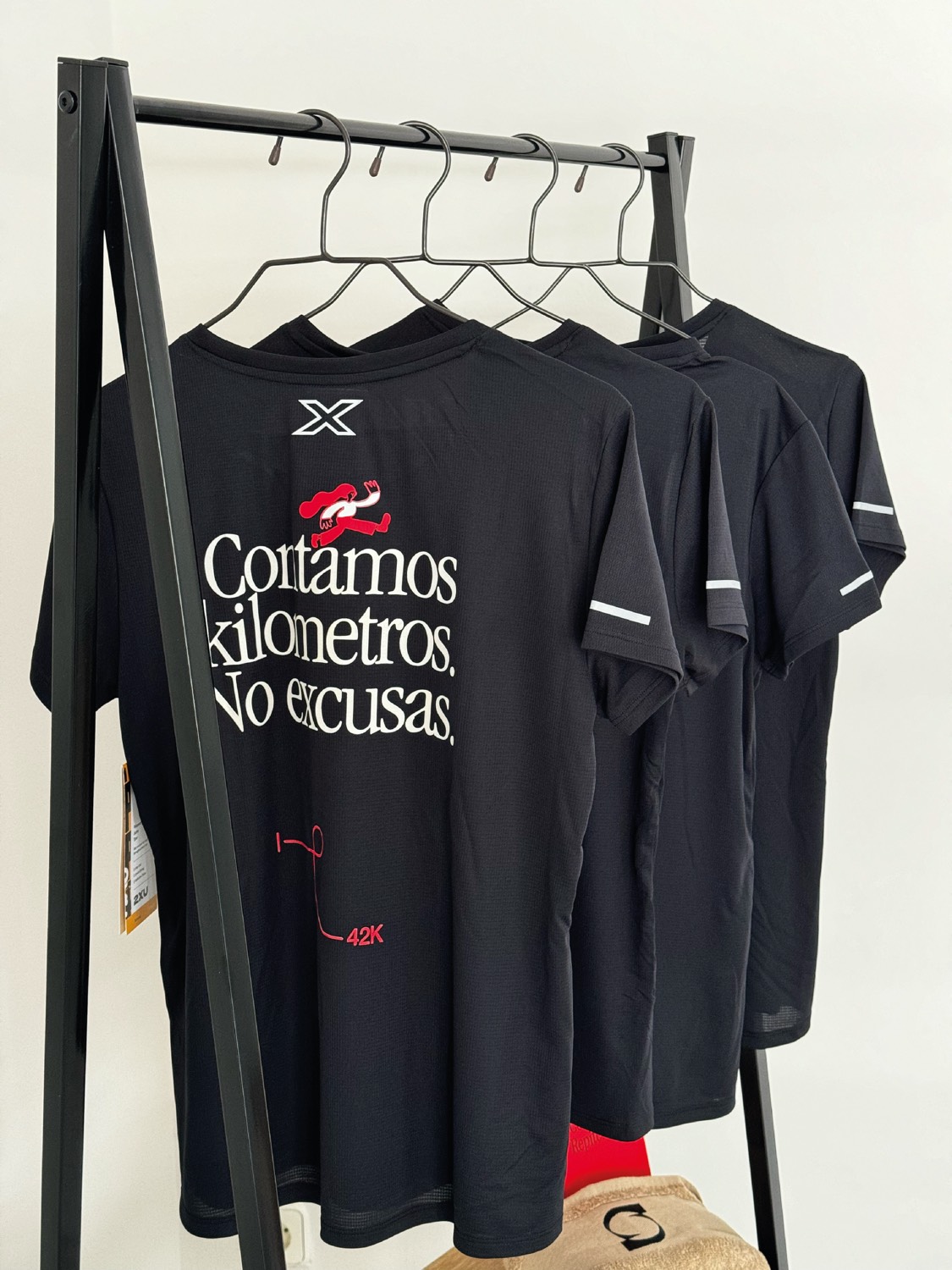 Varias camisetas de manga corta de Sporty Hangover en un perchero, con la frase Contamos kilómetros. No excusas. en la espalda